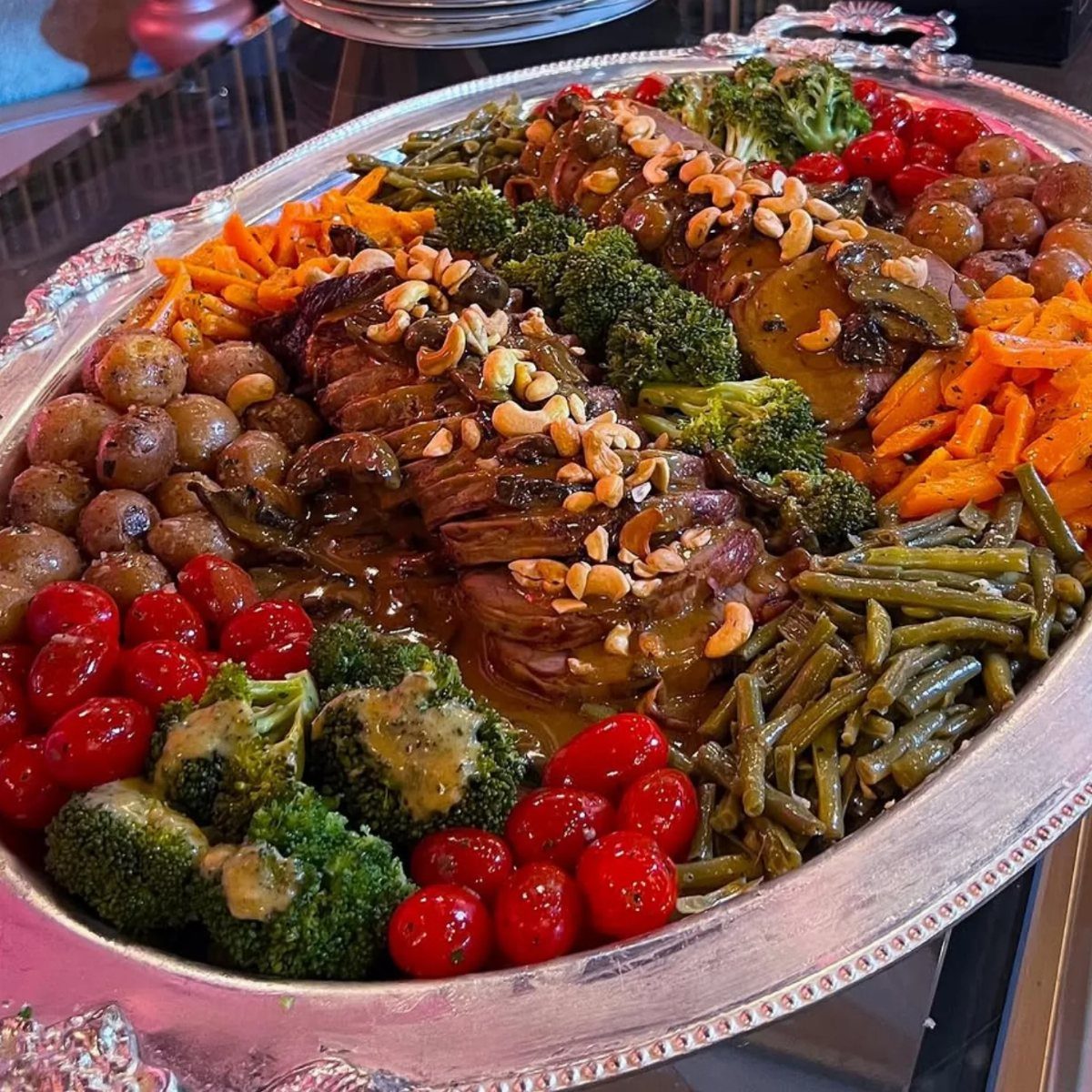 Large silver platter with roast beef, roasted vegetables, and gravy for a dinner party.