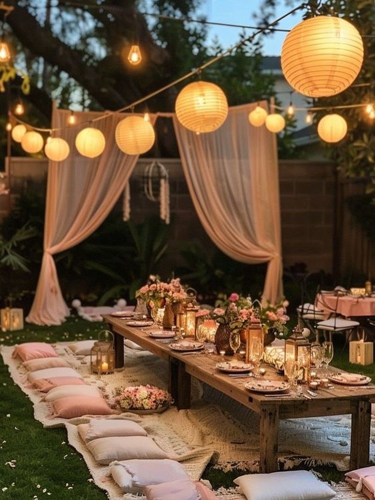 Long wooden dinner table with floral arrangements and lanterns in an outdoor garden