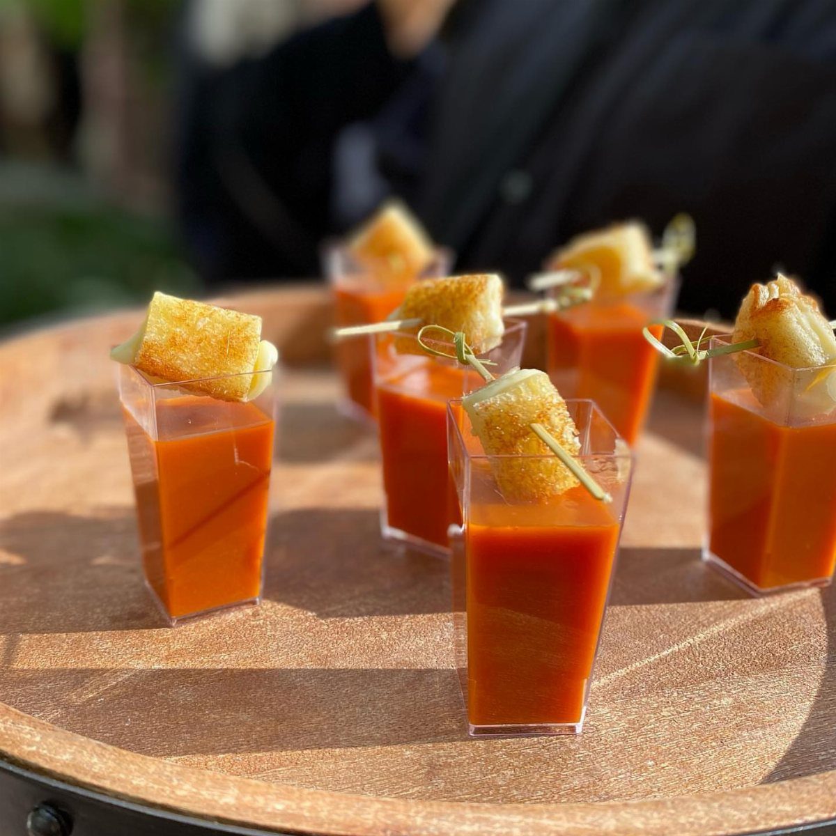 Mini grilled cheese bites perched atop small cups of tomato soup on gold tray
