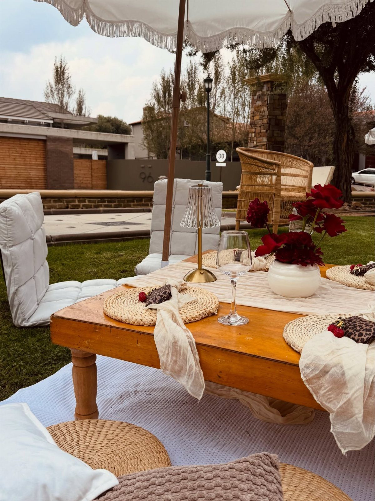 Low wooden dining table with red roses and woven mats on a lawn