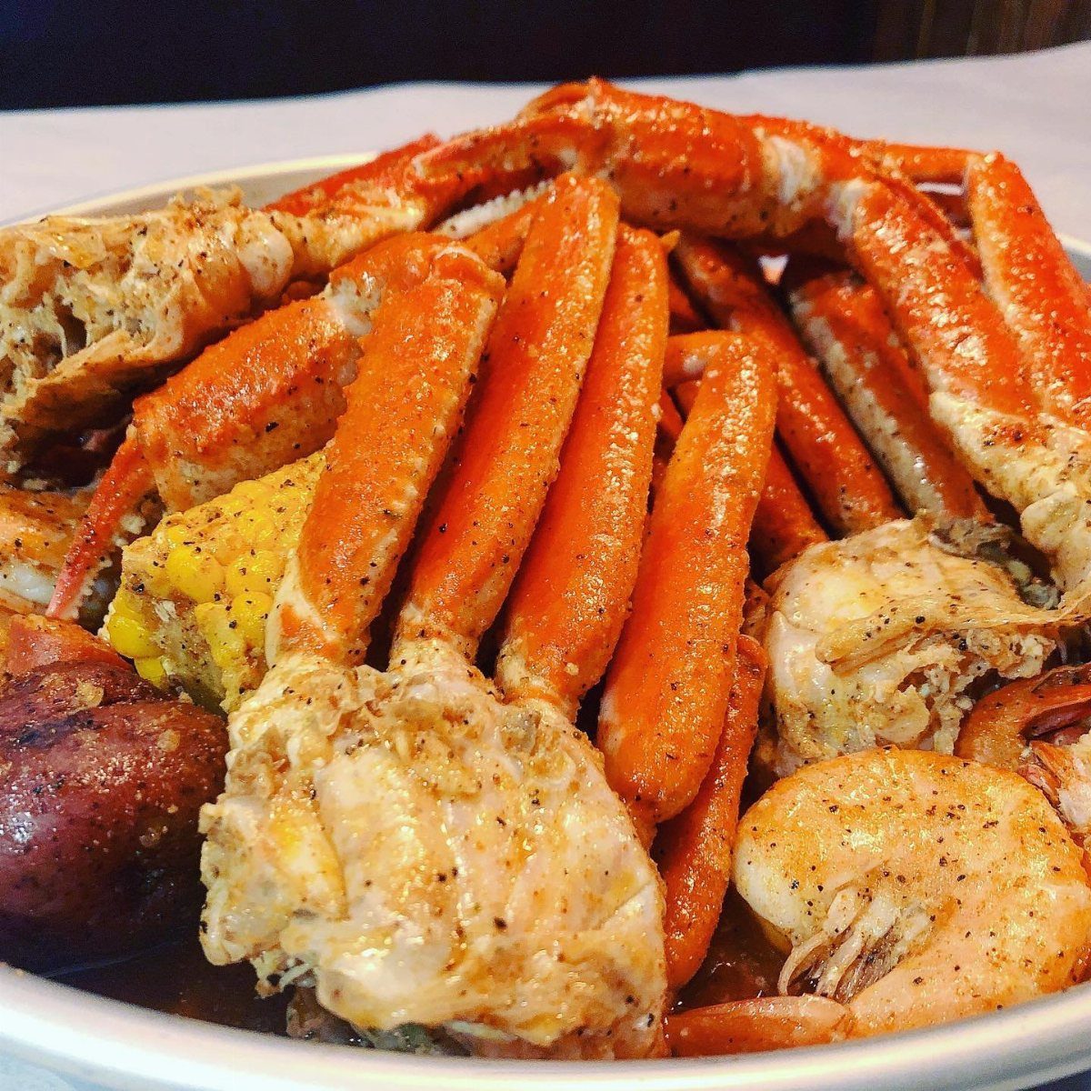 Seafood boil with crab legs, shrimp, corn, and potatoes on a white platter.
