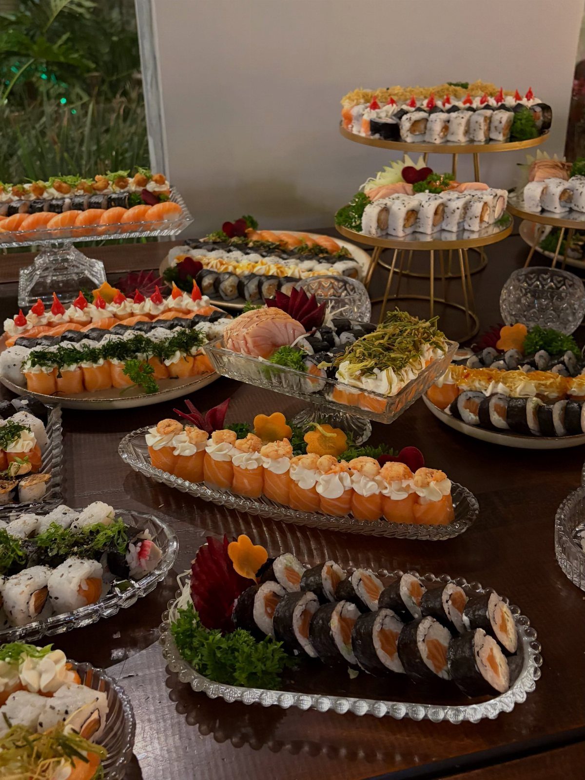 Assorted sushi rolls on glass and gold platters arranged for a party buffet.