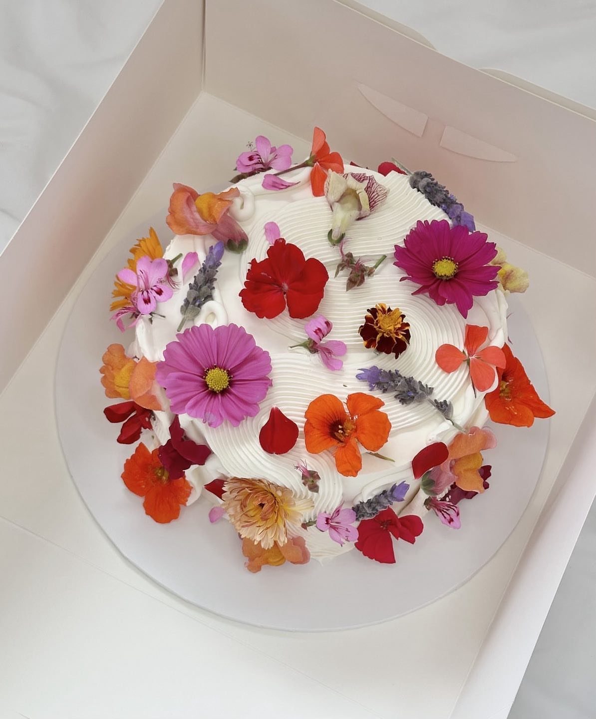 White frosted cake decorated with colorful edible flowers in a white box