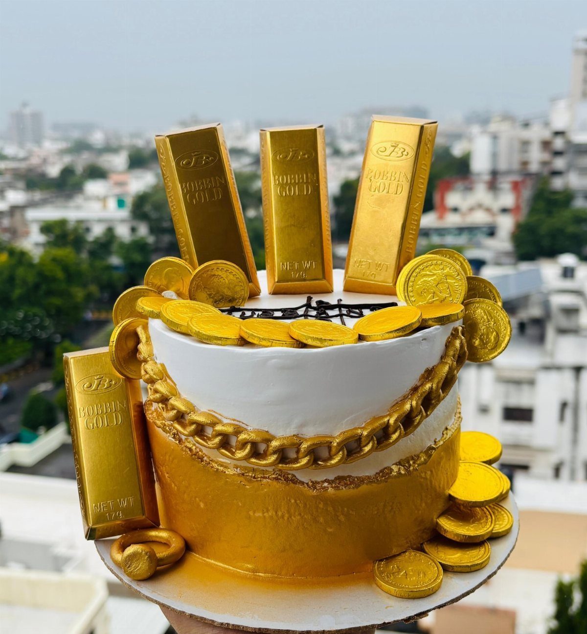 Gold and white cake decorated with edible gold bars, coins, and a chain.