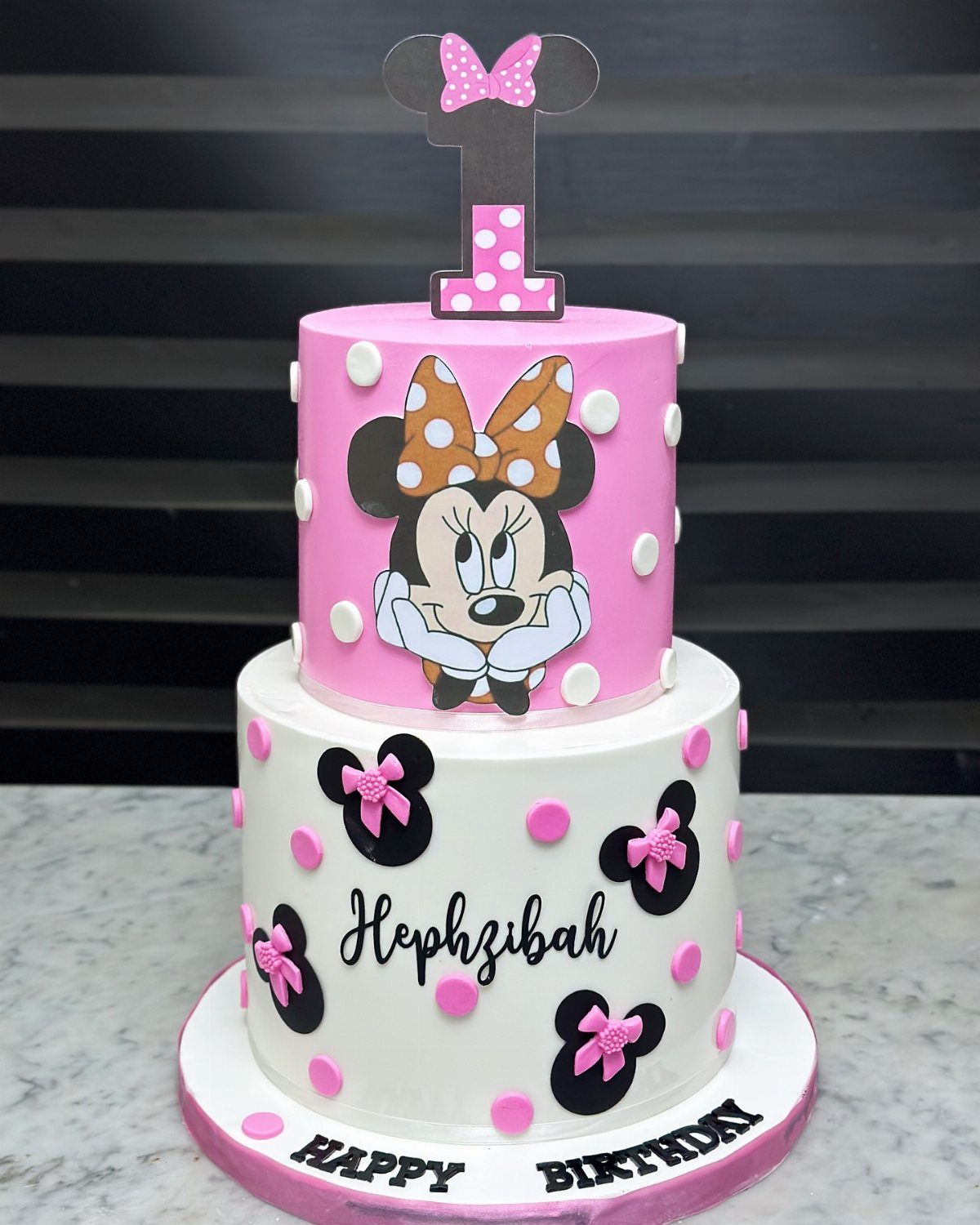 Two-tier Minnie Mouse birthday cake with pink and white frosting and polka dots.