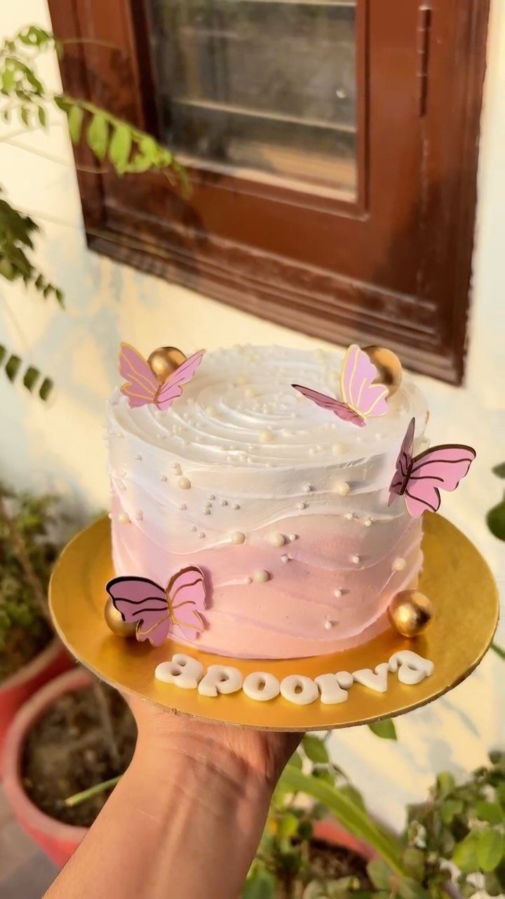 Round cake with pink and white ombre frosting, pink butterflies, and gold spheres.