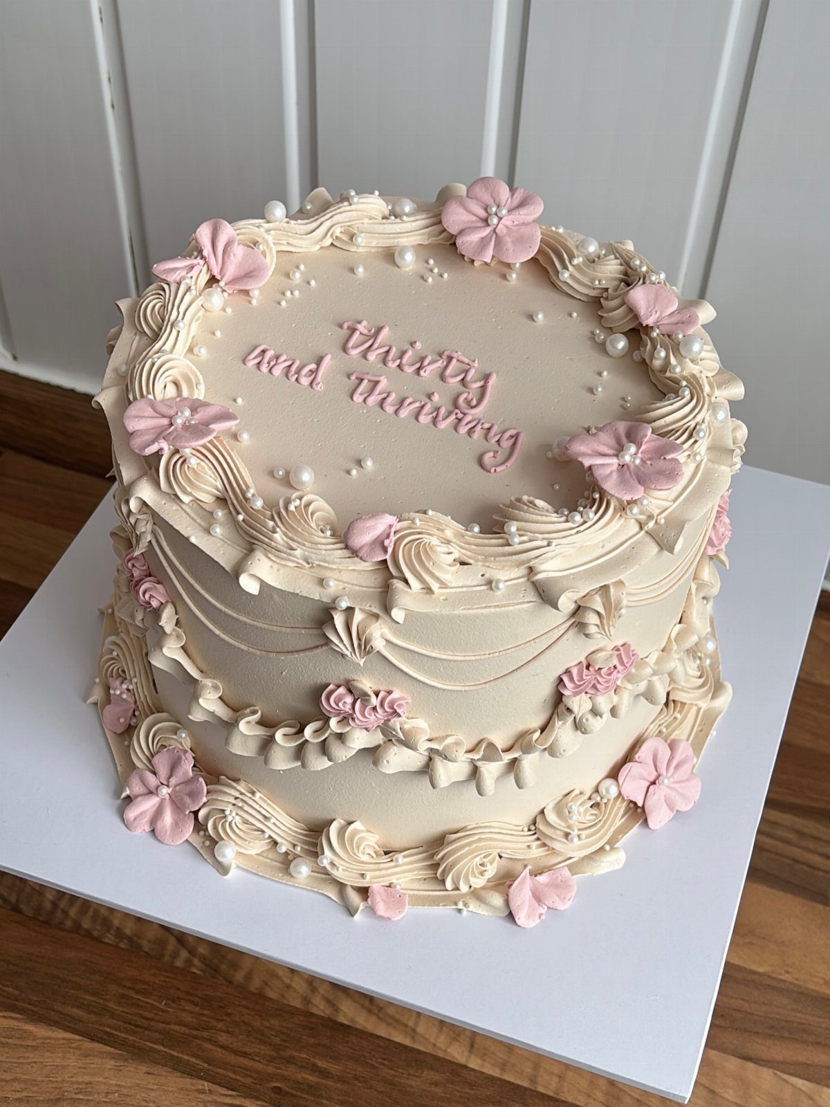 Cream-colored birthday cake with intricate piped frosting ruffles and small pink flowers.