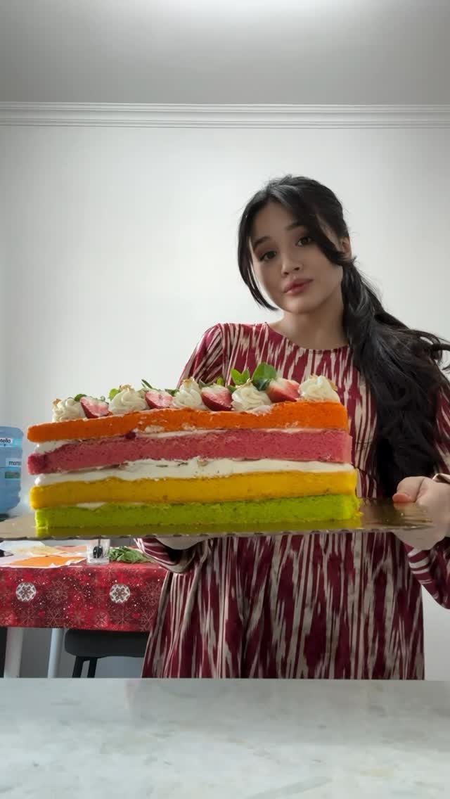 Multi-layered rainbow cake with strawberries held by a woman in red dress