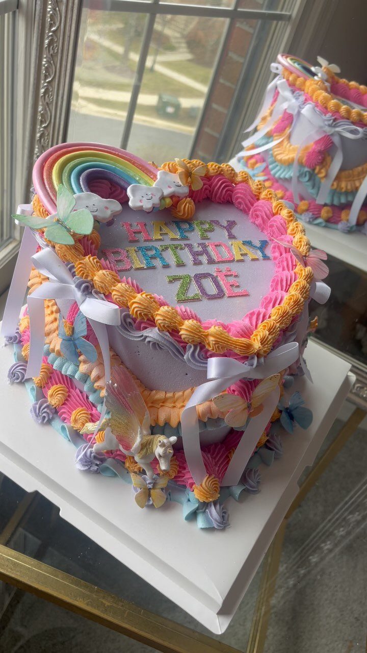 Heart-shaped birthday cake with colorful swirled icing, a rainbow topper, and butterfly decorations.
