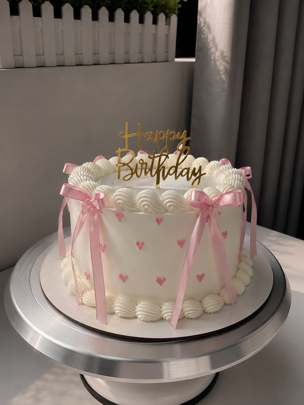 White birthday cake with pink heart sprinkles, pink ribbons, and gold topper.