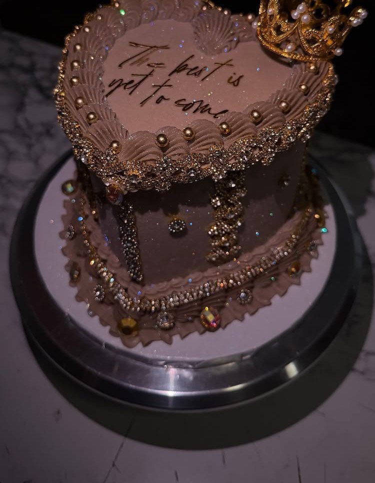 Heart-shaped brown cake adorned with gold beads, crystals, and a small gold crown.