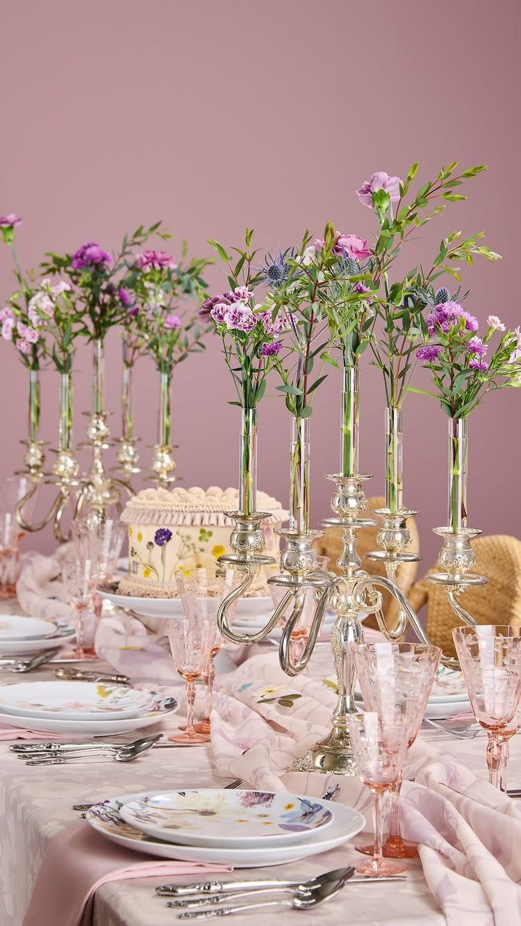 Tall glass bud vases with purple flowers on a decorated cake table.