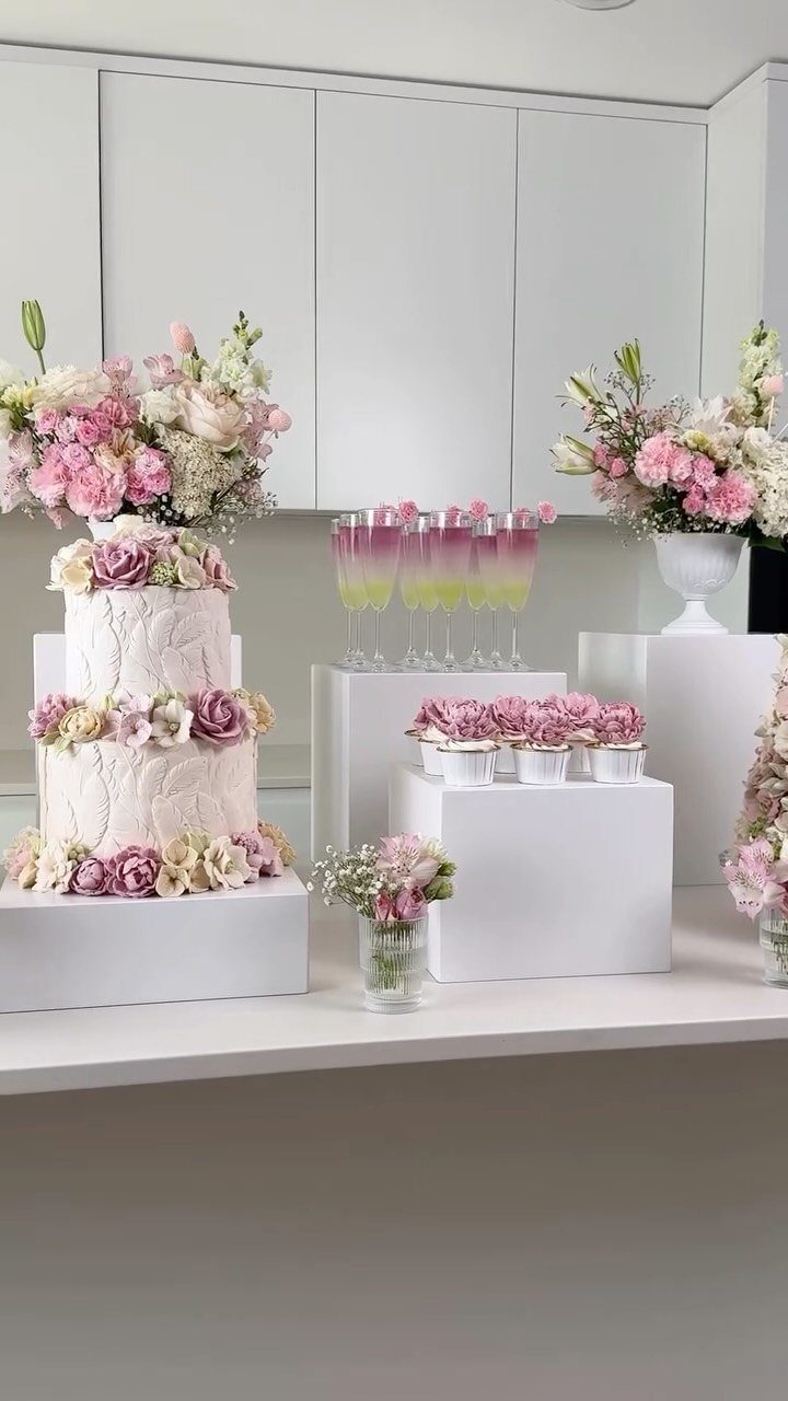 Two-tier white cake decorated with pink flowers on a white dessert table setup.