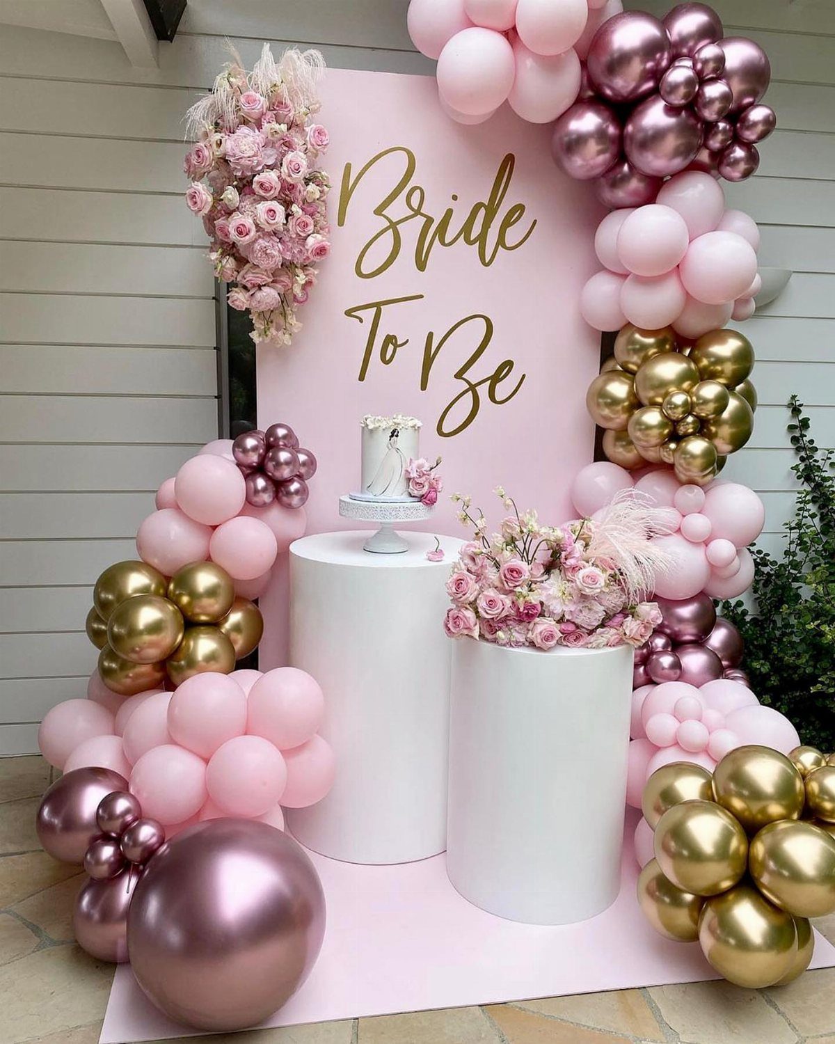 Bridal shower cake table with pink balloons, white pedestals, and pink floral arrangements.