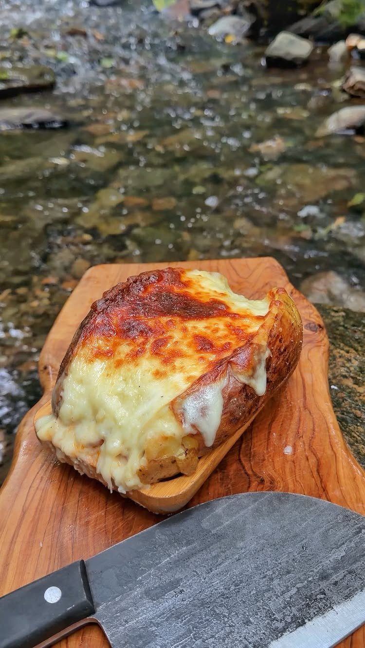 Baked potato with melted cheese on a wooden board by a rocky stream