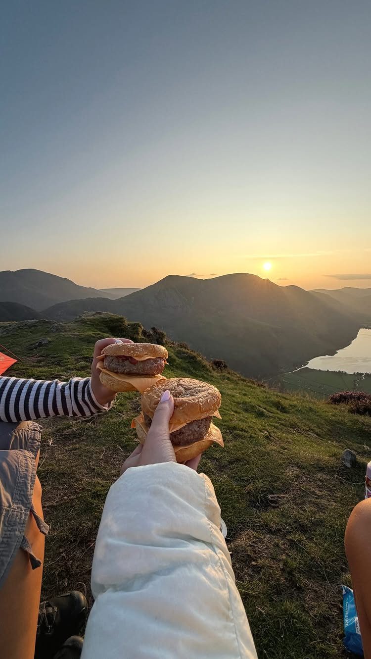 Two hamburgers held up against a sunset mountain landscape and valley view.