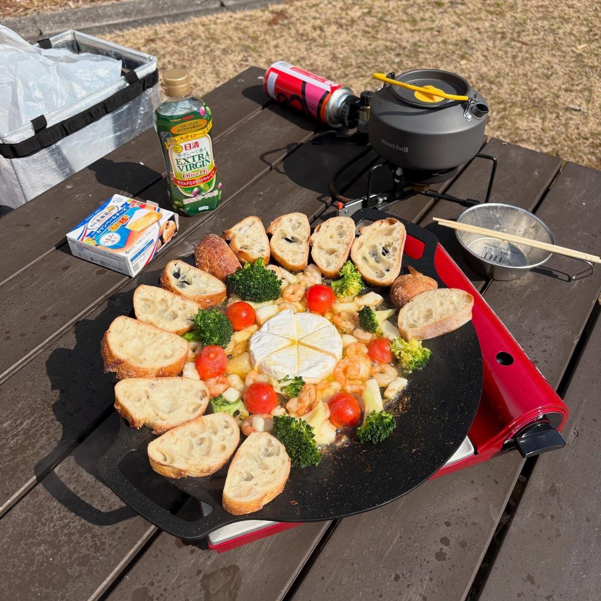 Brie cheese and toasted baguette slices with vegetables on a camping griddle.