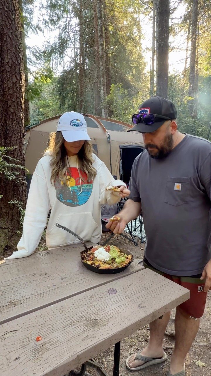Man and woman eating nachos from a cast iron skillet at a campsite.