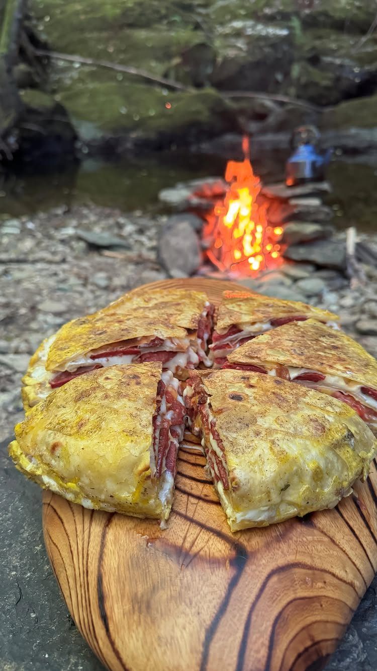 Sliced toasted quesadilla on a wooden board with a campfire in the background