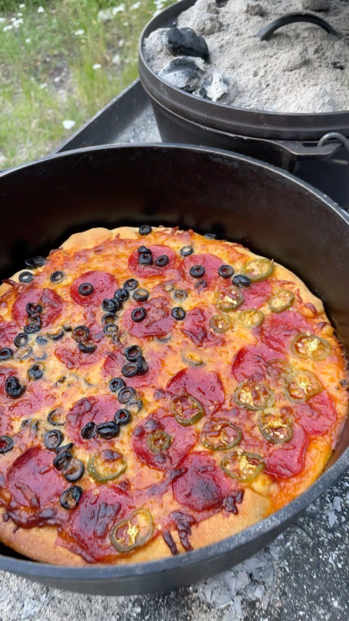 Pepperoni pizza with olives and jalapeños baked inside a black cast iron Dutch oven.