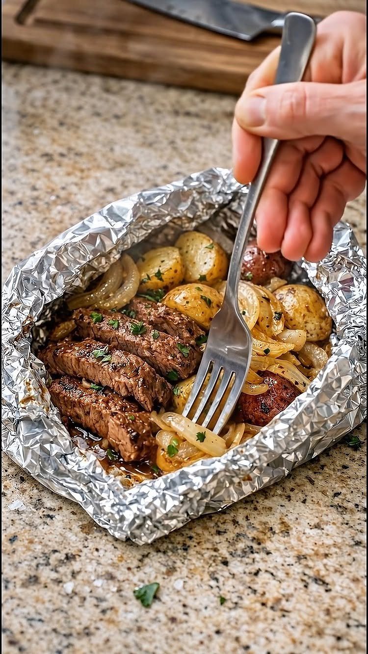 Sliced steak, potatoes, and onions cooked in an aluminum foil packet on granite.