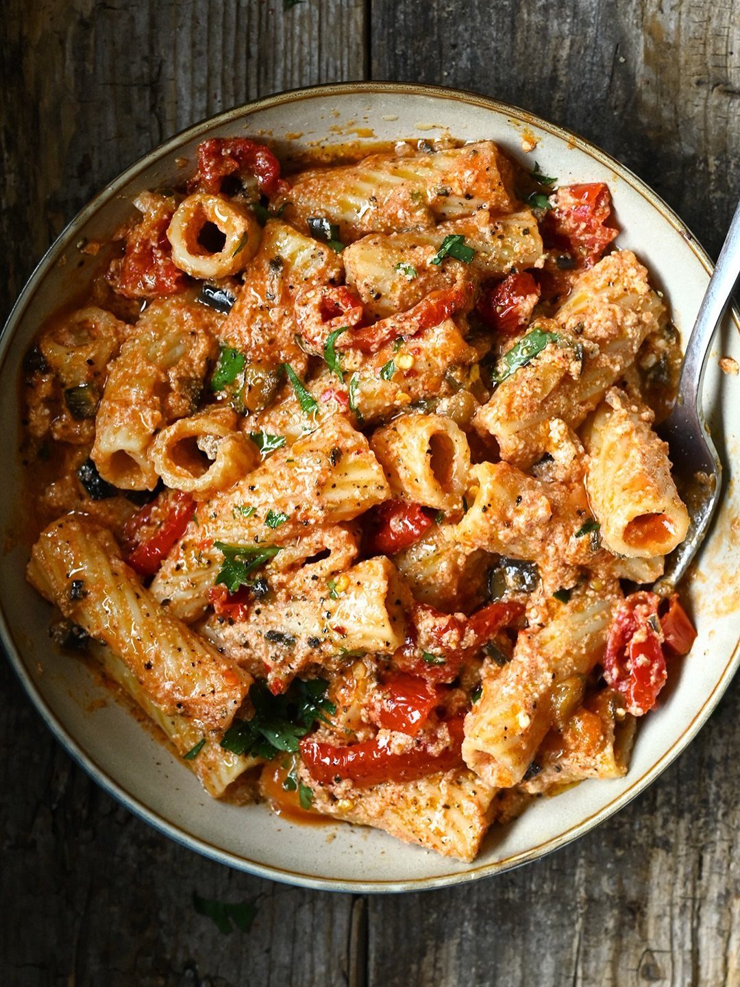 Rigatoni pasta with creamy tomato sauce and herbs in a white bowl.