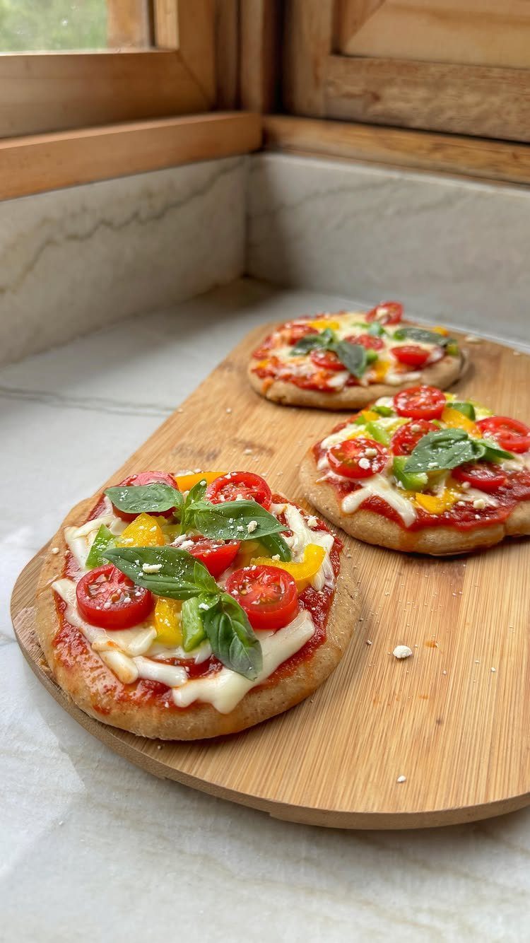 Three pita bread pizzas with cheese, tomatoes, and basil on a wooden board.