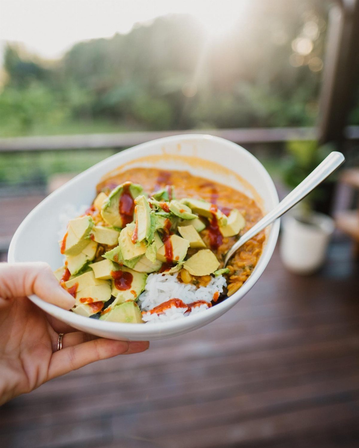 Rice bowl with beans, diced avocado, and red sauce held over wooden deck.