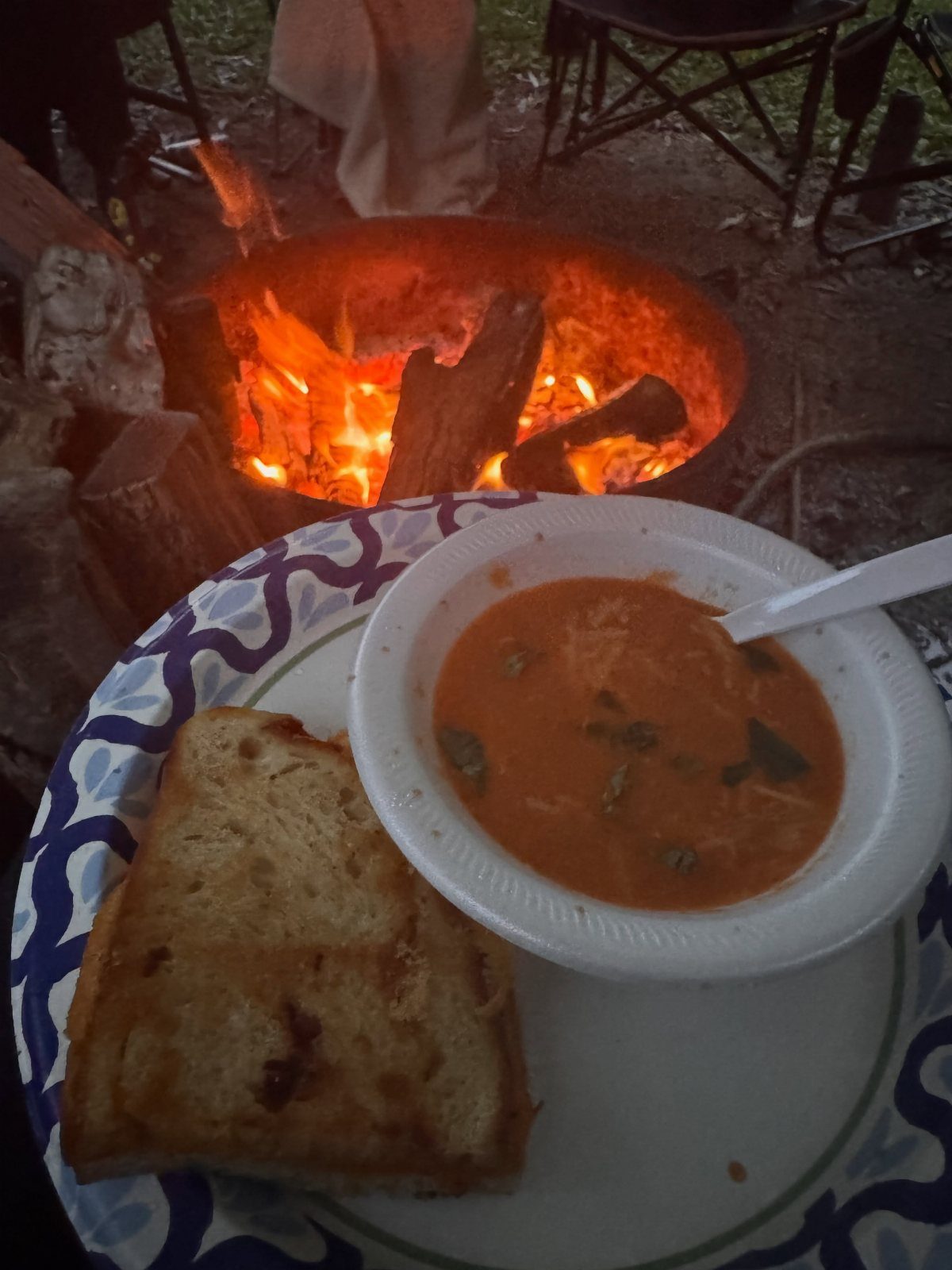 Bowl of orange soup and toasted bread served outdoors by a campfire.