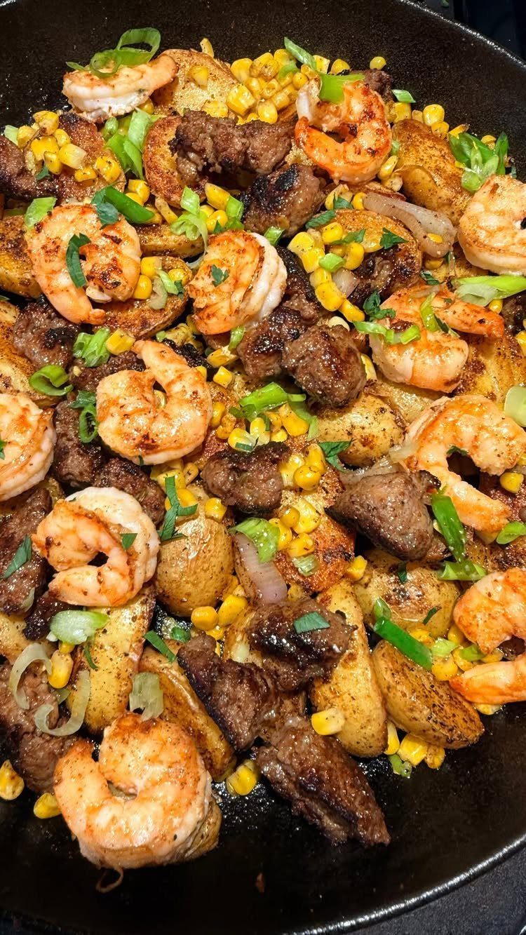 Shrimp, beef, and roasted potatoes with corn in a black cast iron skillet.