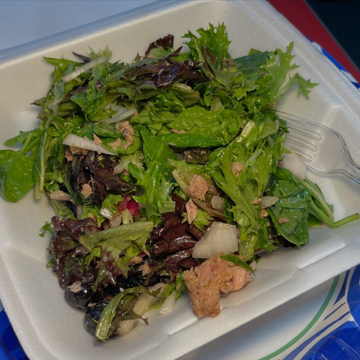 Tuna salad with mixed greens and onions in a white foam container.