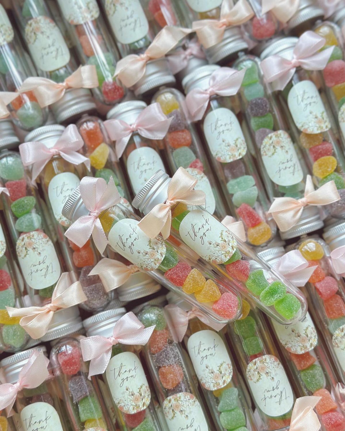 Small glass jars filled with colorful gummy candies, tied with pink ribbons and labels.