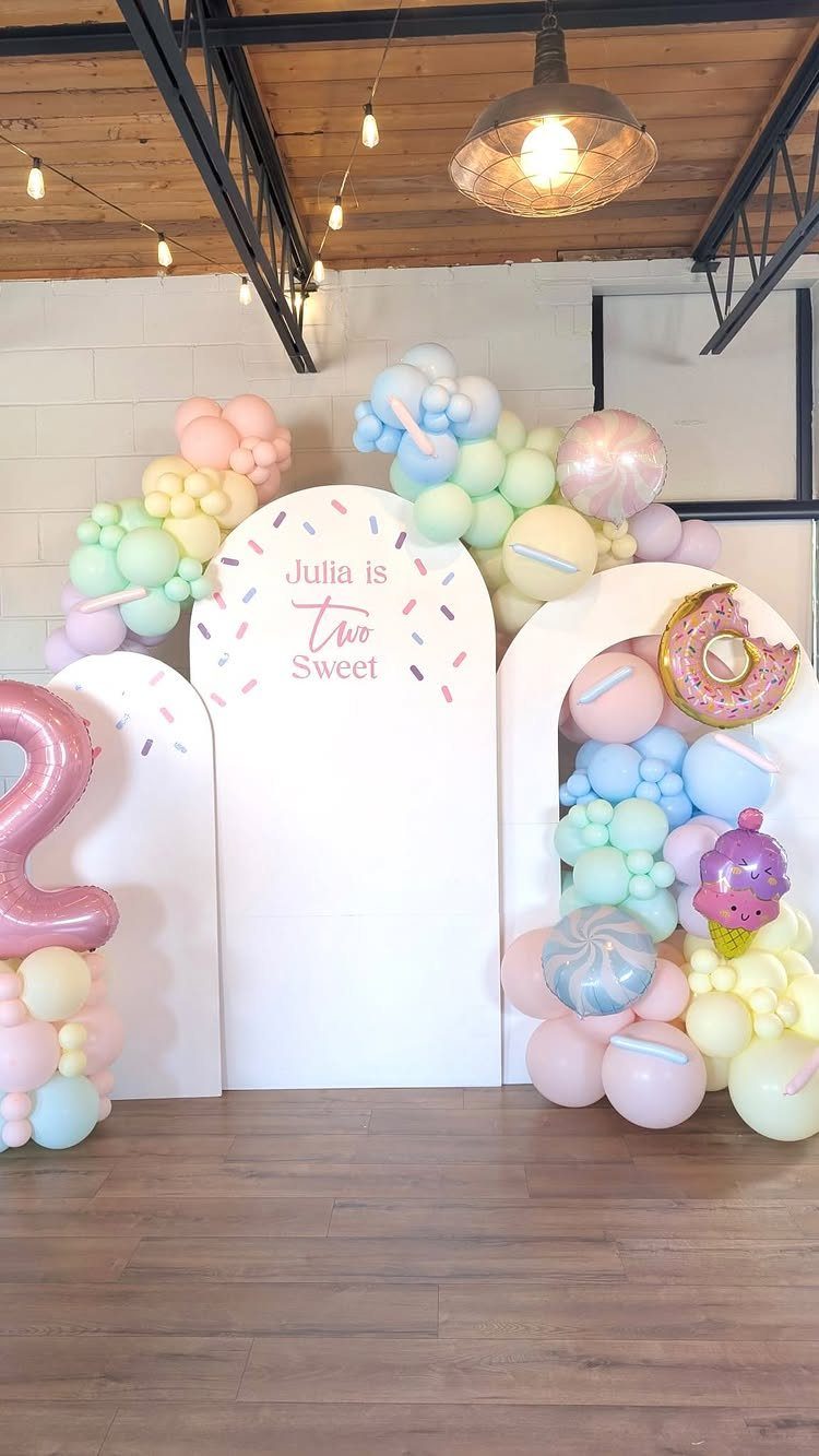 White arched backdrop with pastel balloons and sweets decorations for a second birthday.