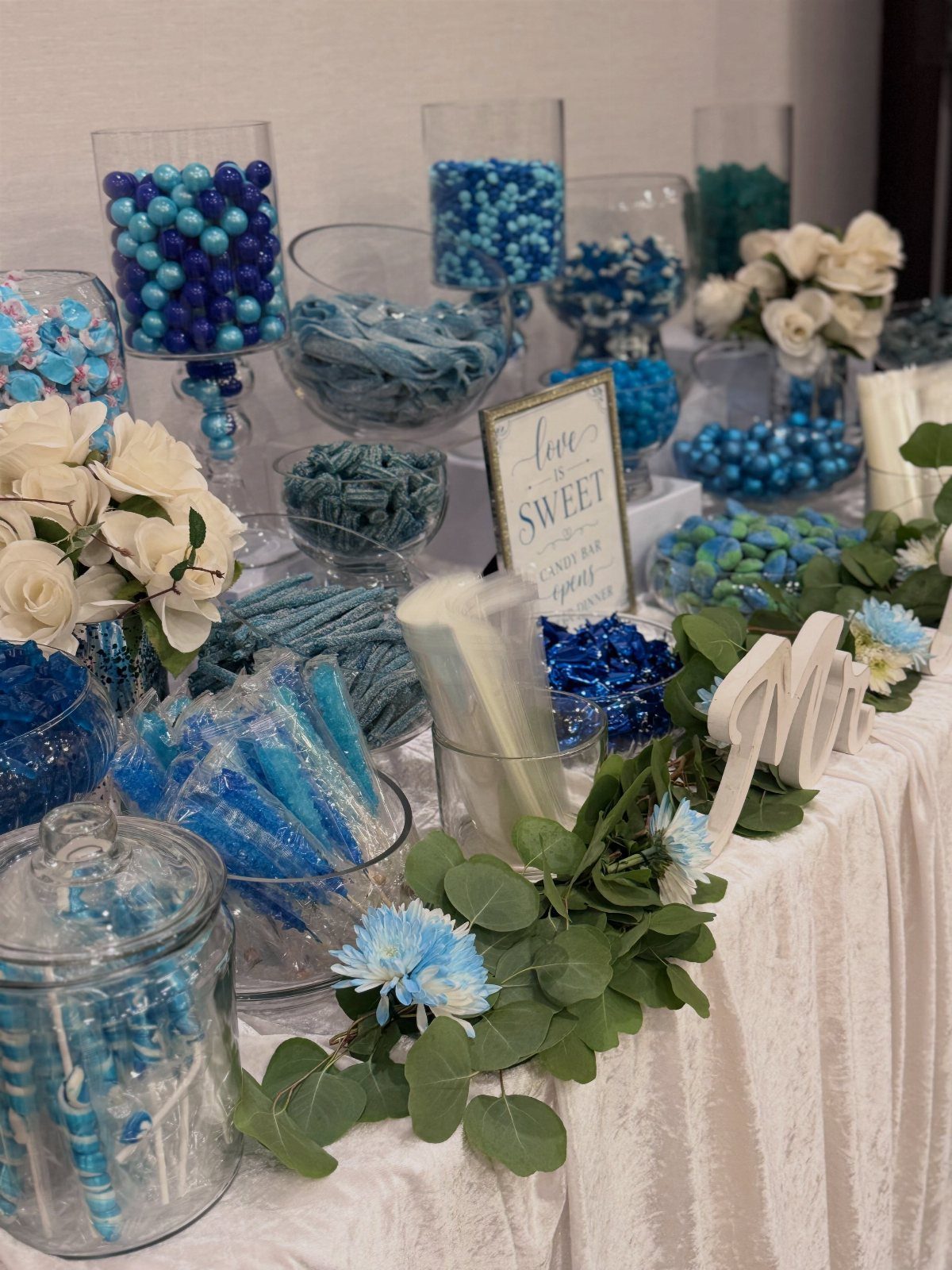 Blue and white candies in glass jars on a white decorated table.