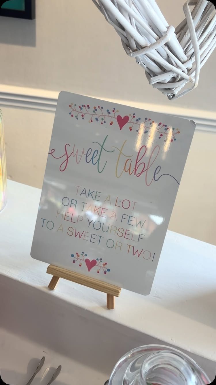 White sweet table sign on a wooden easel with colorful lettering and hearts.