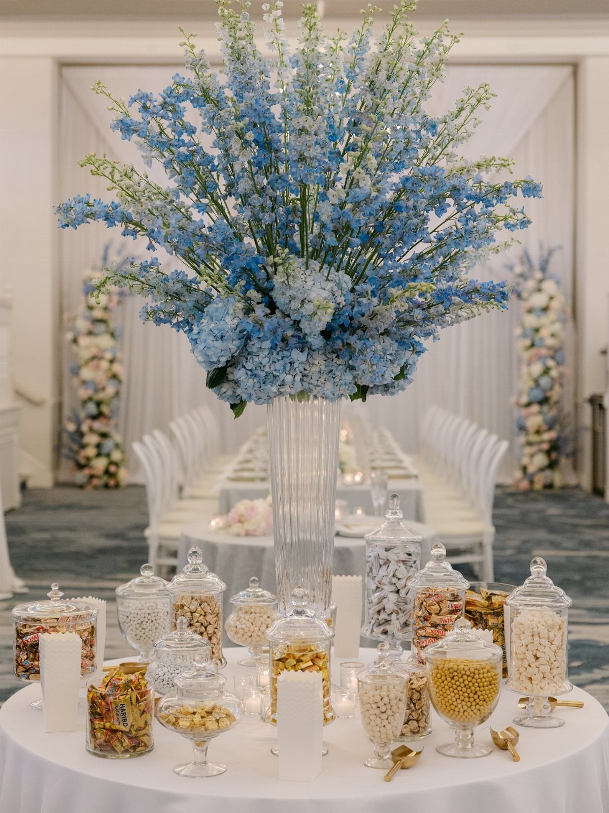 Candy table with glass jars of sweets and a tall blue floral centerpiece.