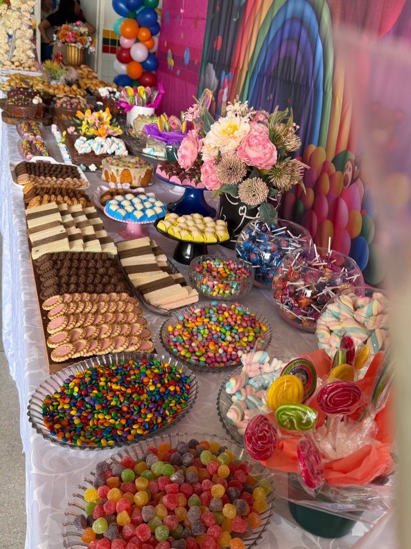 Colorful candy table with sweets in glass bowls and a rainbow backdrop.