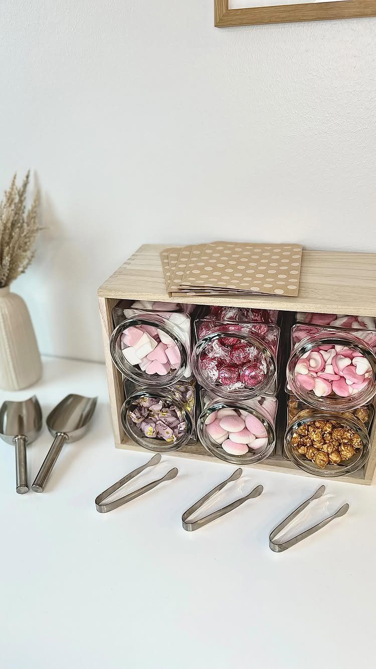 Candy station with glass bowls of sweets, metal scoops, tongs, and paper bags.