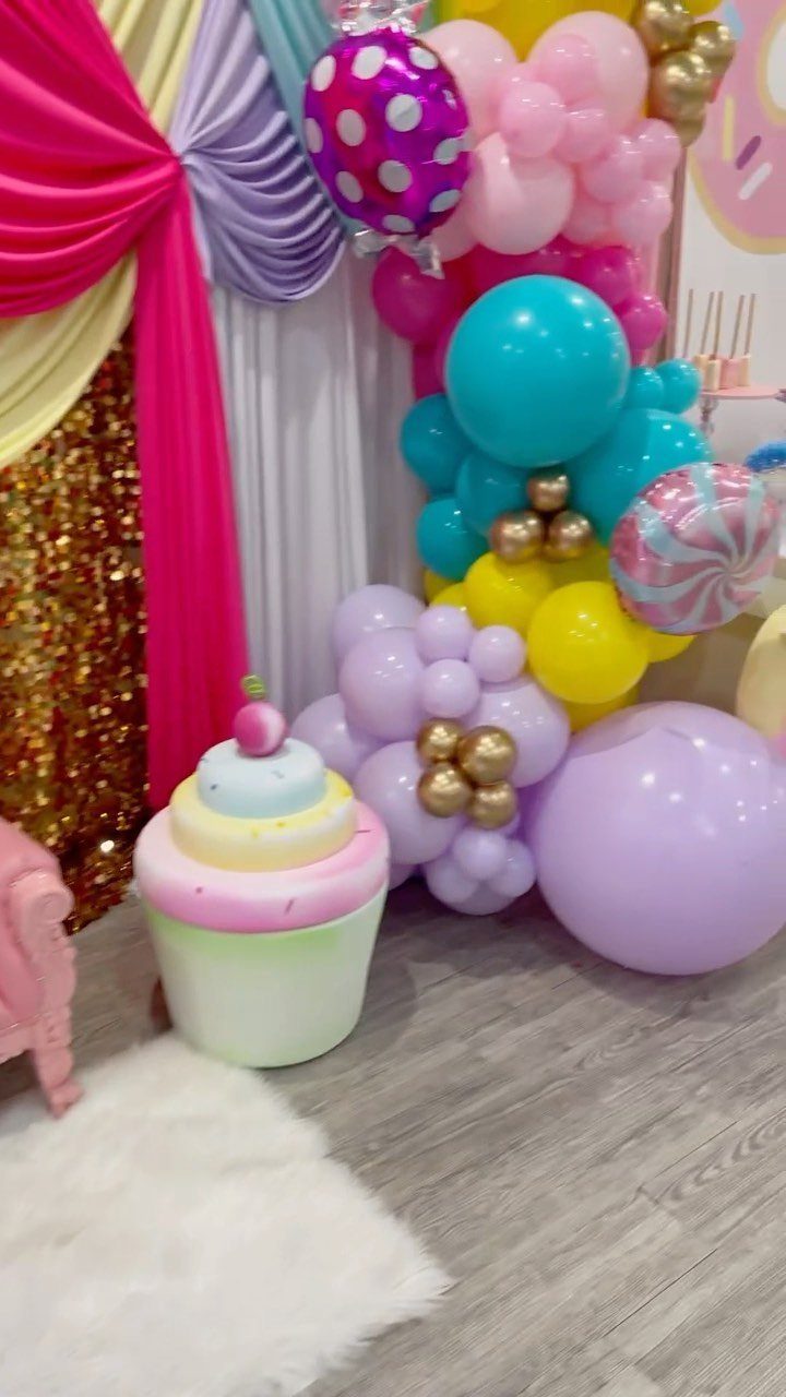 Cupcake prop and colorful balloon arch against sequined and draped fabric backdrops.