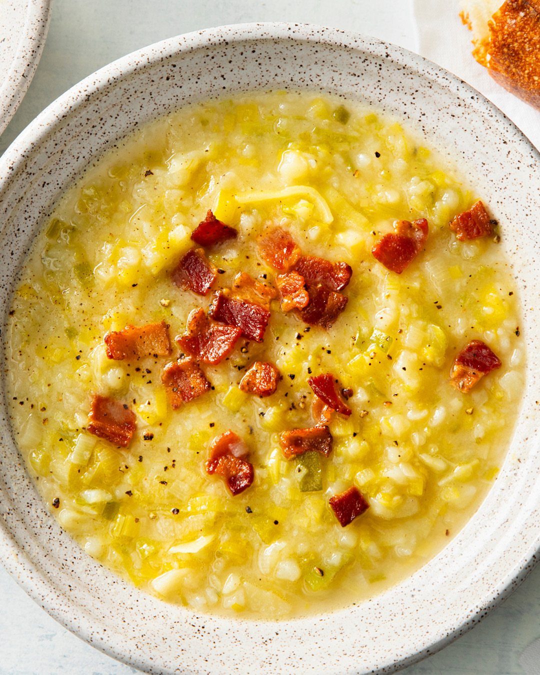 Creamy potato leek soup in a white bowl topped with crispy bacon bits.