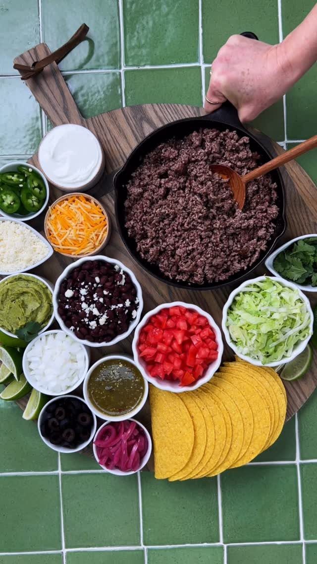 Taco bar spread with ground meat, taco shells, and various colorful toppings on wood.