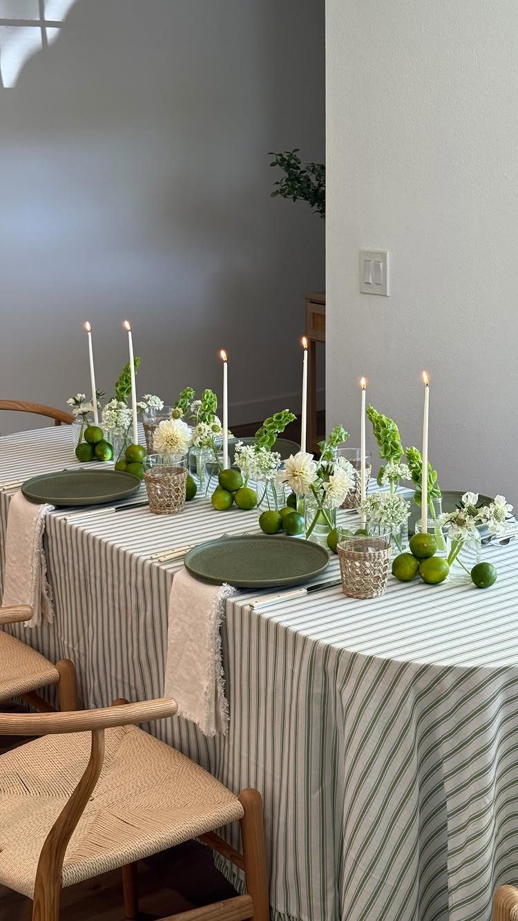 Dining table set with green plates, white candles, and limes on striped cloth.