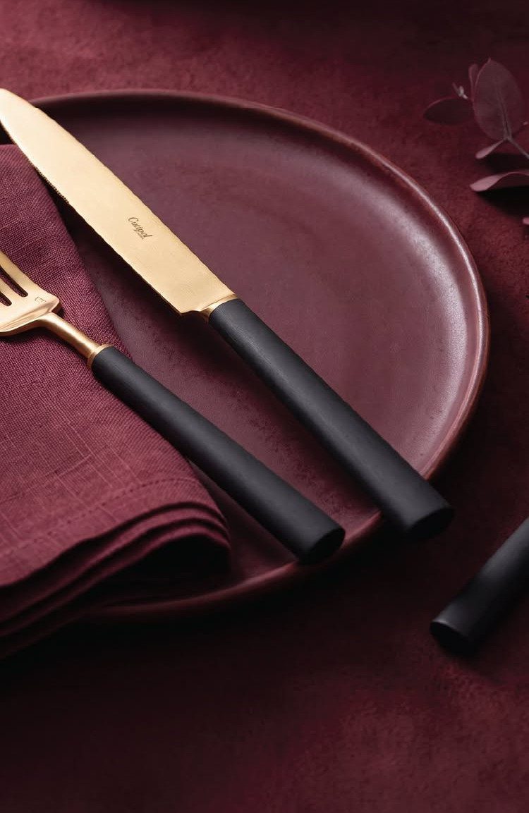Gold cutlery with black handles on a burgundy plate and matching napkin.