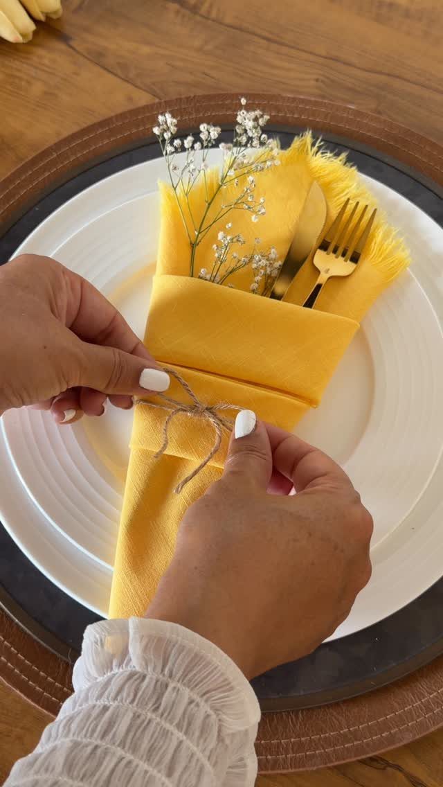 Hands tying a twine bow on a yellow napkin with gold cutlery.