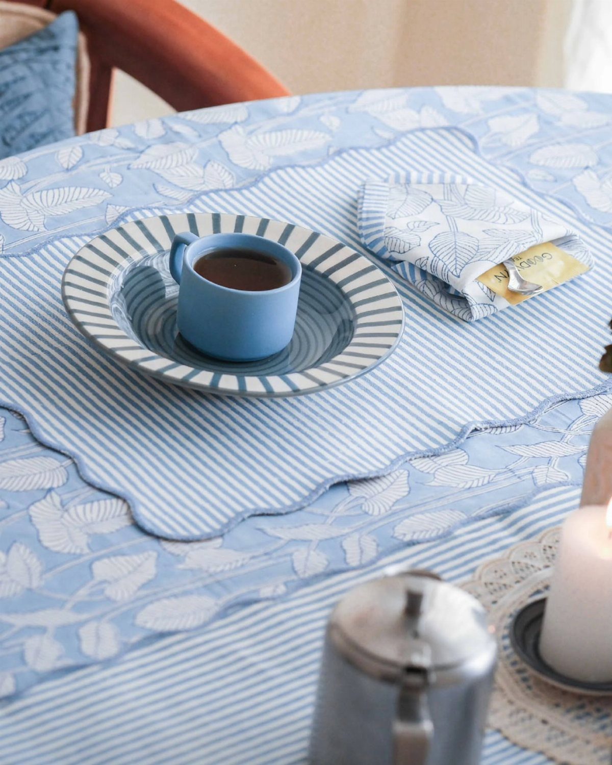 Blue coffee cup and saucer on a striped runner and floral tablecloth.