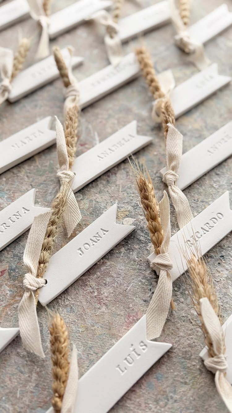 White name cards tied with beige ribbons and wheat stalks on grey stone.