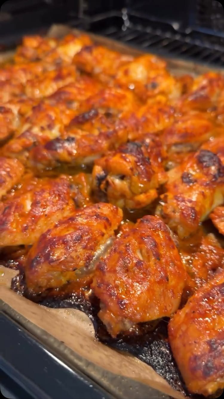 Glazed chicken wings with charred edges on parchment paper in an oven tray.