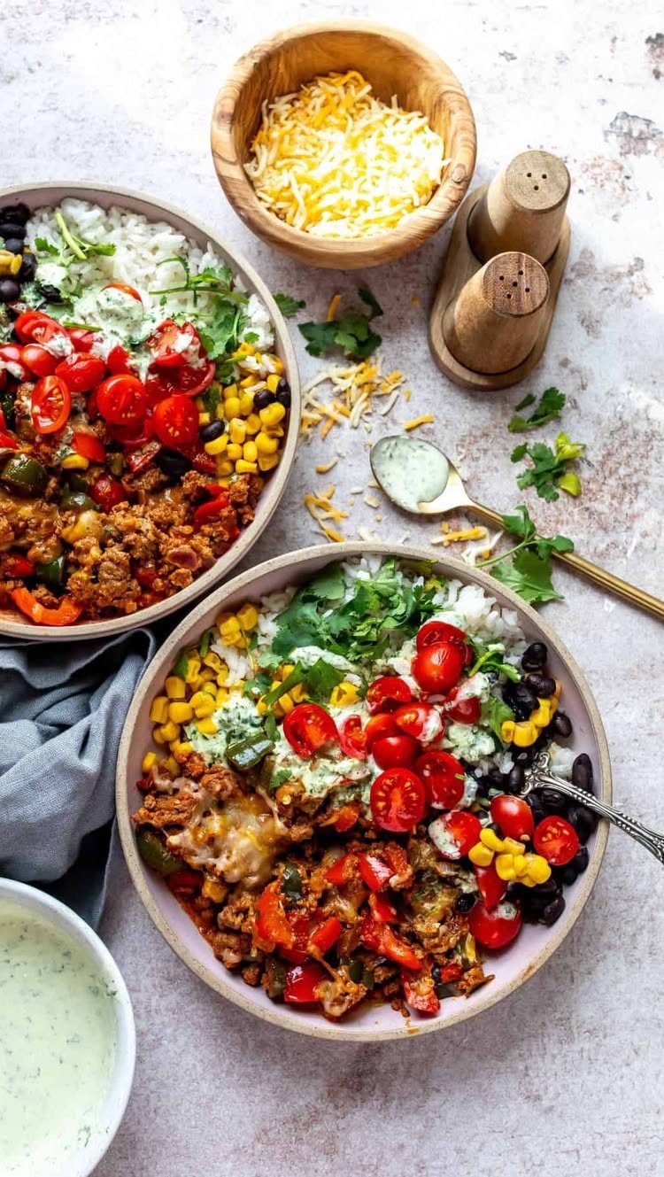Two burrito bowls with rice, meat, corn, beans, and tomatoes on a table.