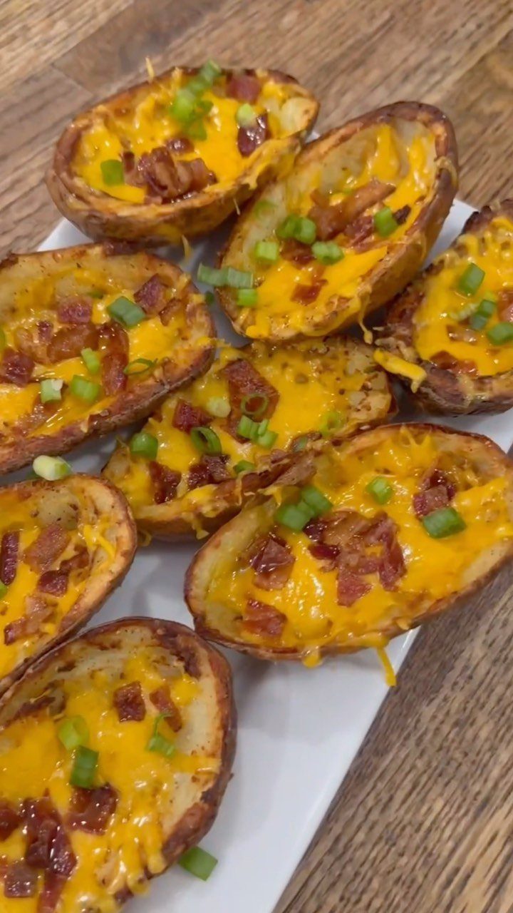 Potato skins topped with melted cheese, bacon bits, and green onions on a platter.