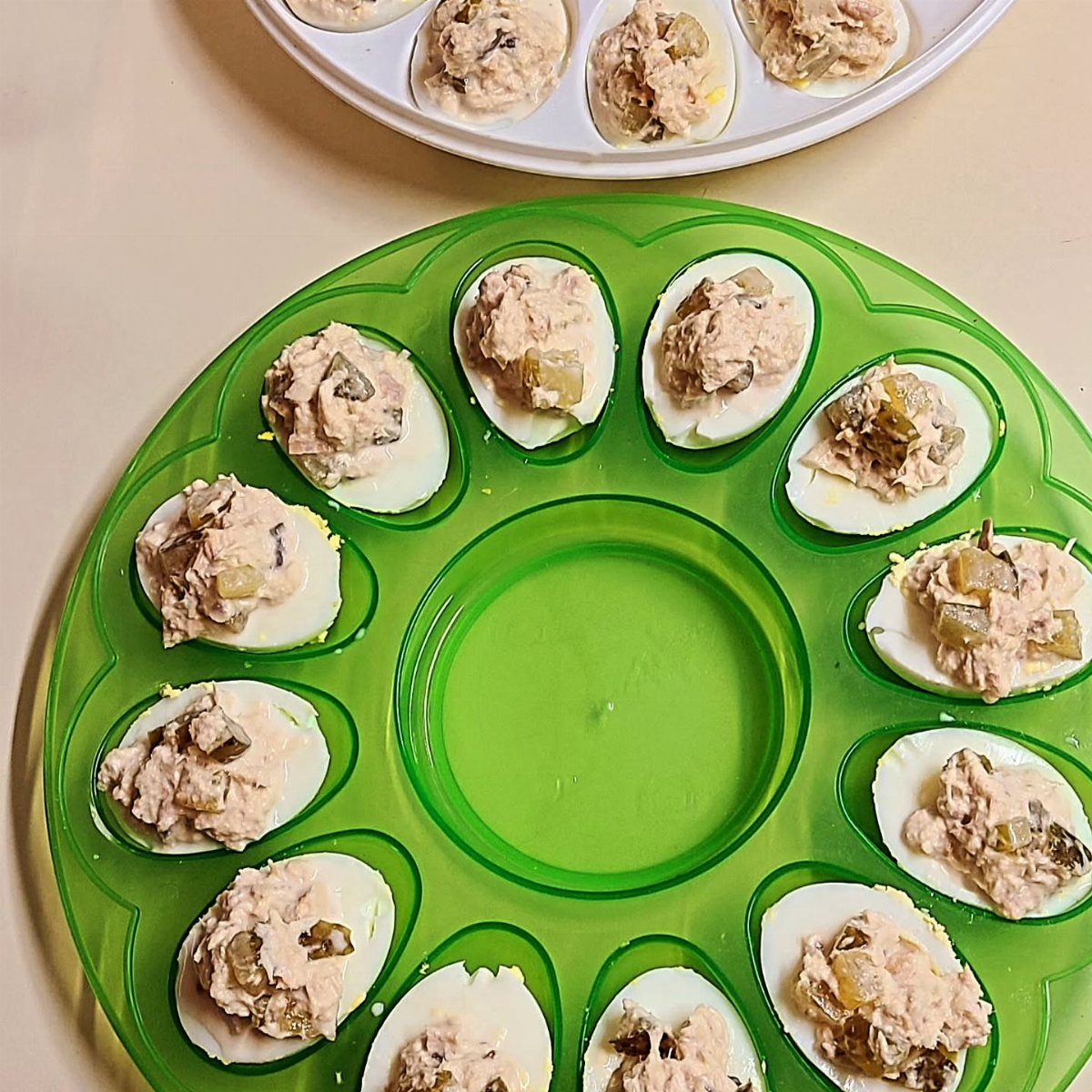 Deviled eggs filled with creamy salad arranged on a green circular plastic tray.